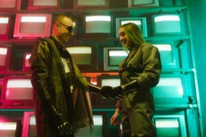 Futuristic scene of two adults shaking hands with prosthetics against a retro TV backdrop.
