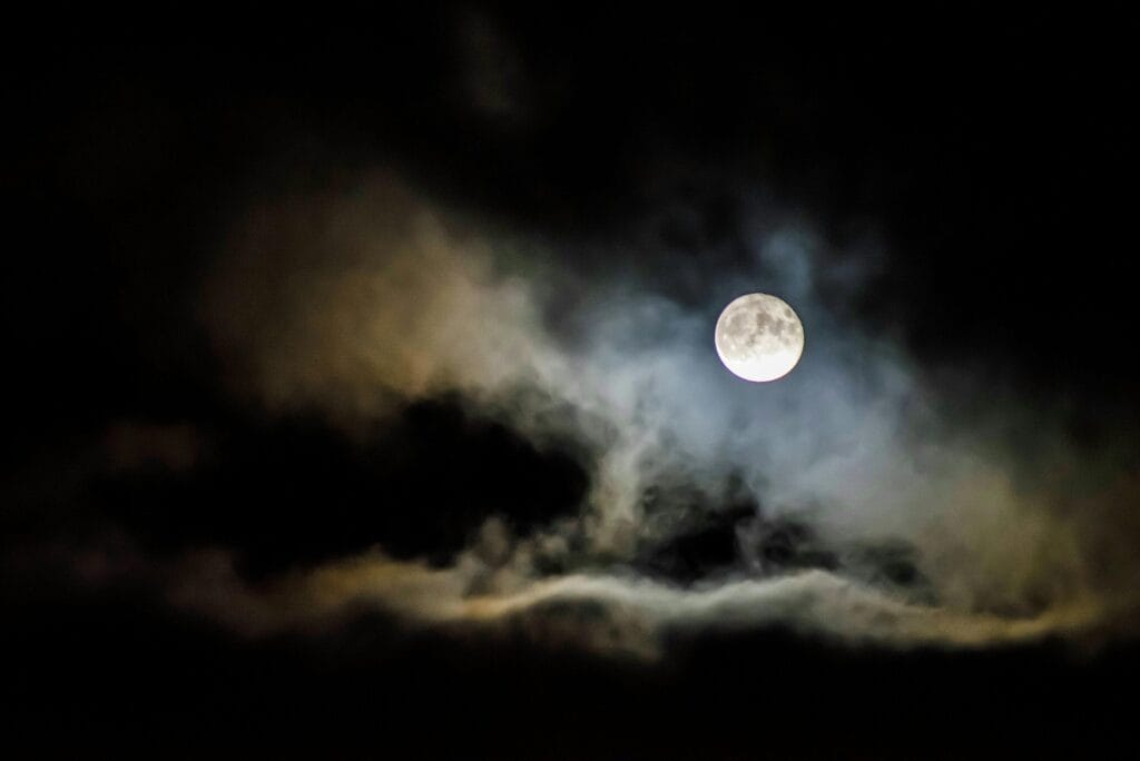 A full moon illuminates the night sky, shrouded by eerie clouds creating a spooky atmosphere.