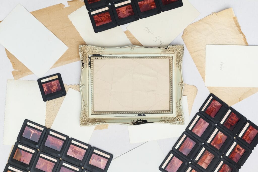 A collection of vintage film slides and an ornate picture frame arranged on old paper.